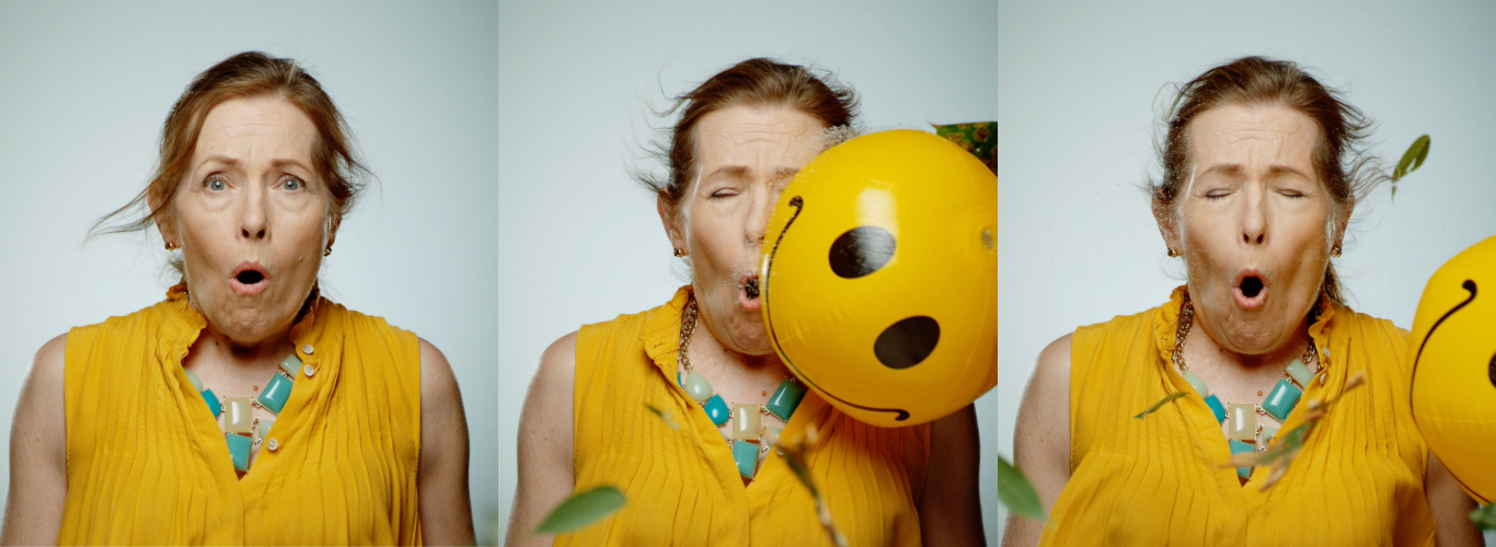 A series of three images of a woman wearing a yellow summer top and blue jewellery. In the first image the woman looks concerned, in the second image she is being hit in the face with a smiley-faced beachball and in the third image the beach ball is bouncing off her face.